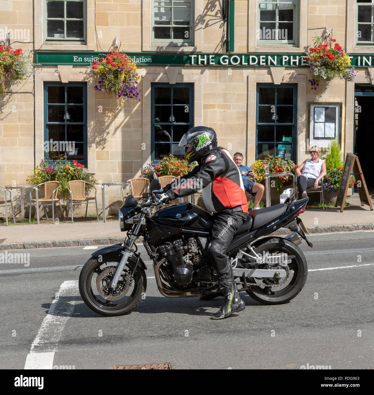Motociclista nella donna, sfondo, bere inn pub The Oxfordshire città di Burford, Inghilterra, Regno Unito. Popolare attrazione turistica vicino a Cotswolds Foto Stock