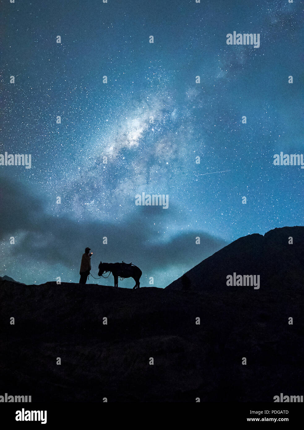 Cavalieri di sostare sotto milioni di stelle in cielo con il suo cavallo vicino fumante vulcano Monte Bromo di notte, Indonesia Foto Stock