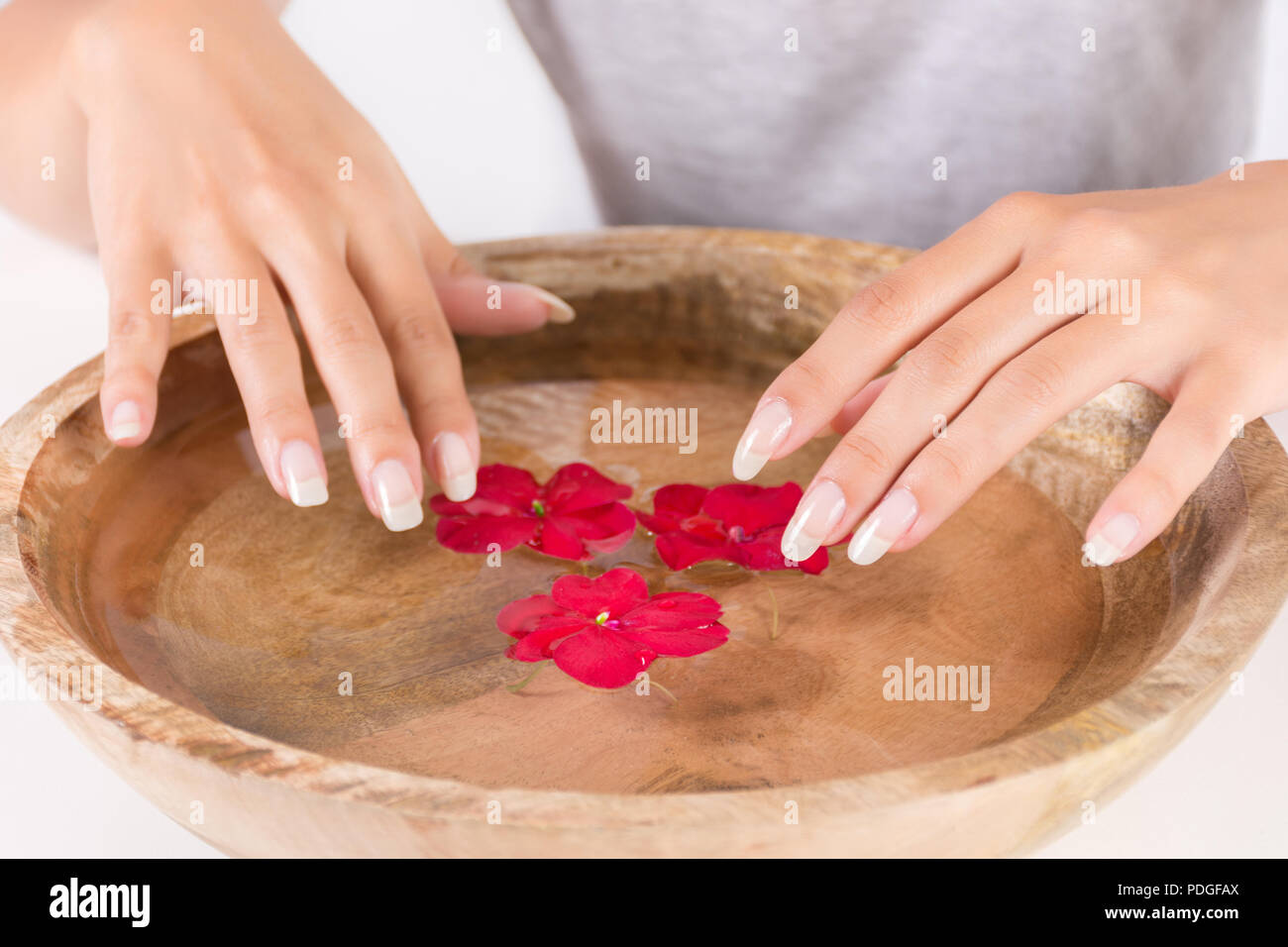 Bellissima femmina naturale unghie manicure e ciotola di legno con acqua e fiore rosso. Trattamento Spa per mani concetto. Close up, il fuoco selettivo Foto Stock