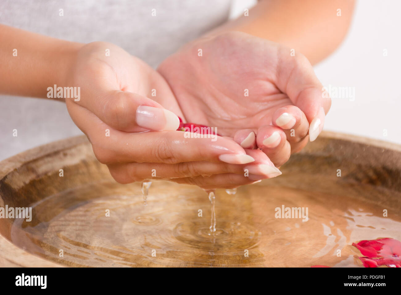 Donna bella mano con manicure naturale sulle unghie contenente acqua in mani e gocce d'acqua nella ciotola di legno. Trattamento Spa per mani concetto Foto Stock