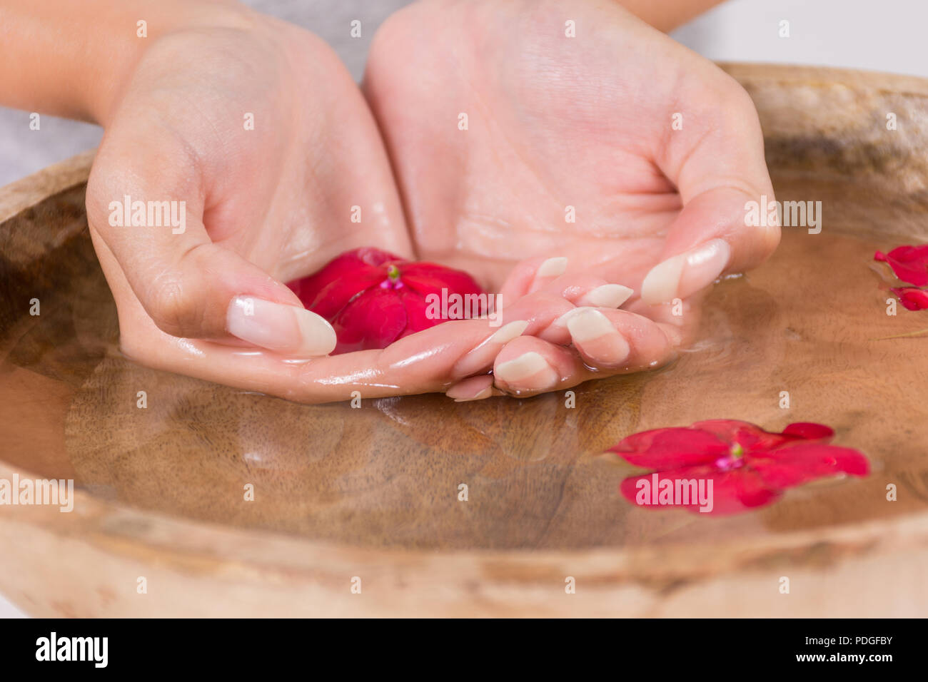 Giovane ragazza mano nella ciotola di legno con acqua e fiore rosso, manicure naturale sulle unghie. Trattamento Spa per mani concetto. Close up, il fuoco selettivo Foto Stock