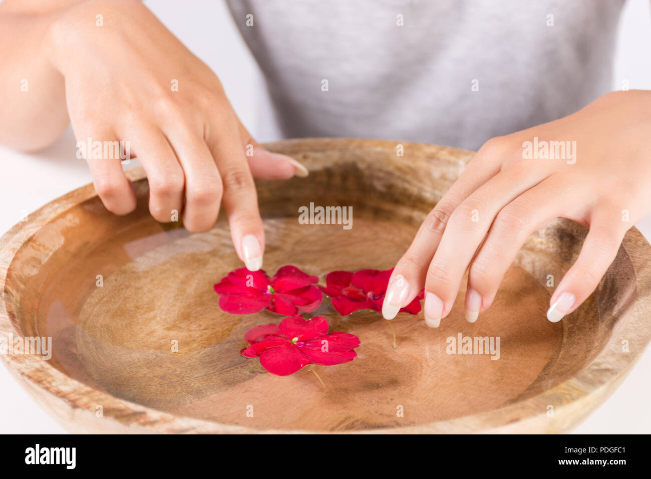 Ragazza giovane con le mani manicure naturale sul dito unghie e ciotola di legno con acqua e fiore. Trattamento Spa per mani concetto. Close up Foto Stock