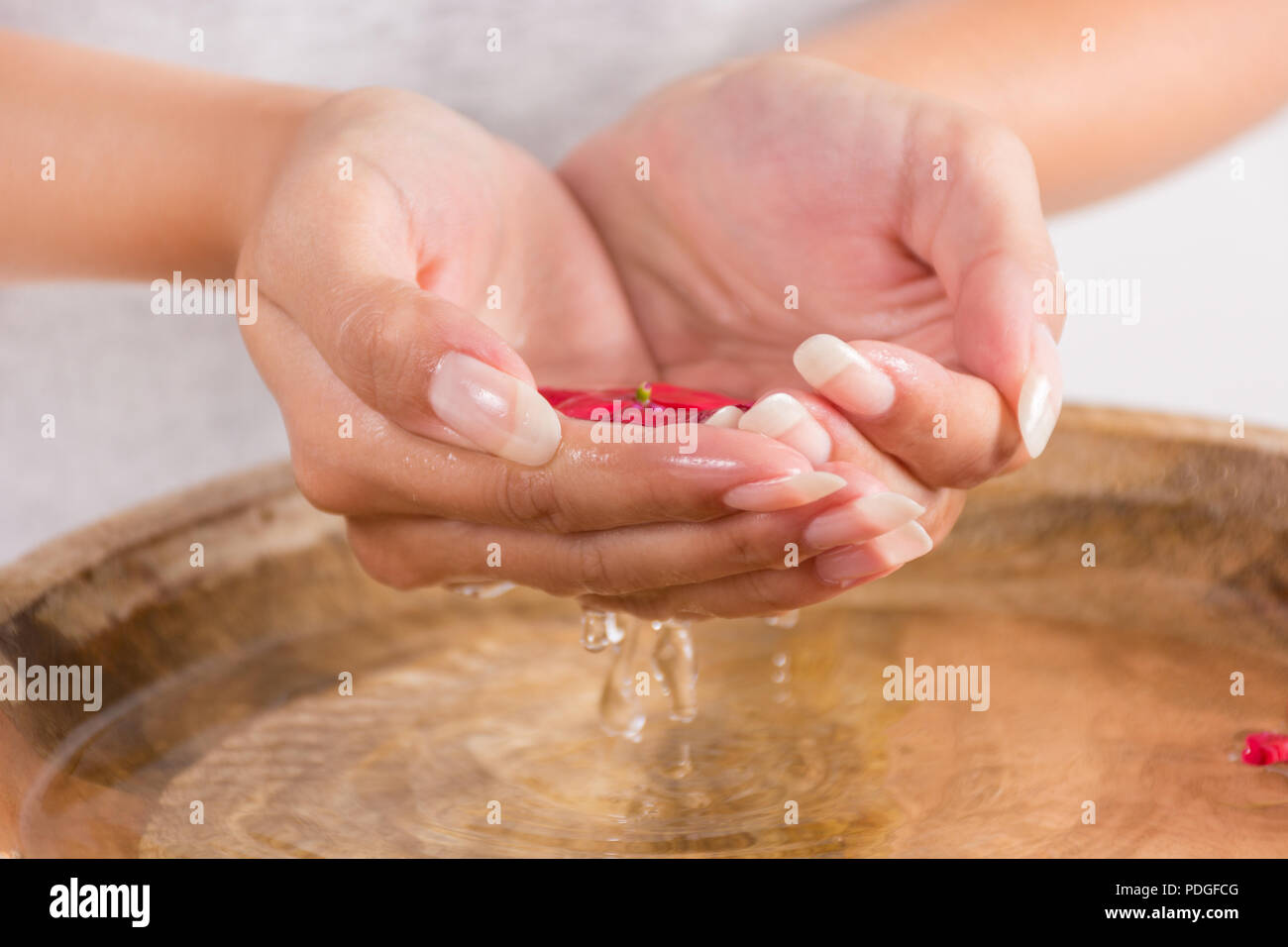 Ragazza giovane con manicure naturale sul dito unghie con acqua in mani e gocce cadono nella ciotola di legno. Trattamento Spa per mani concetto. Close up Foto Stock