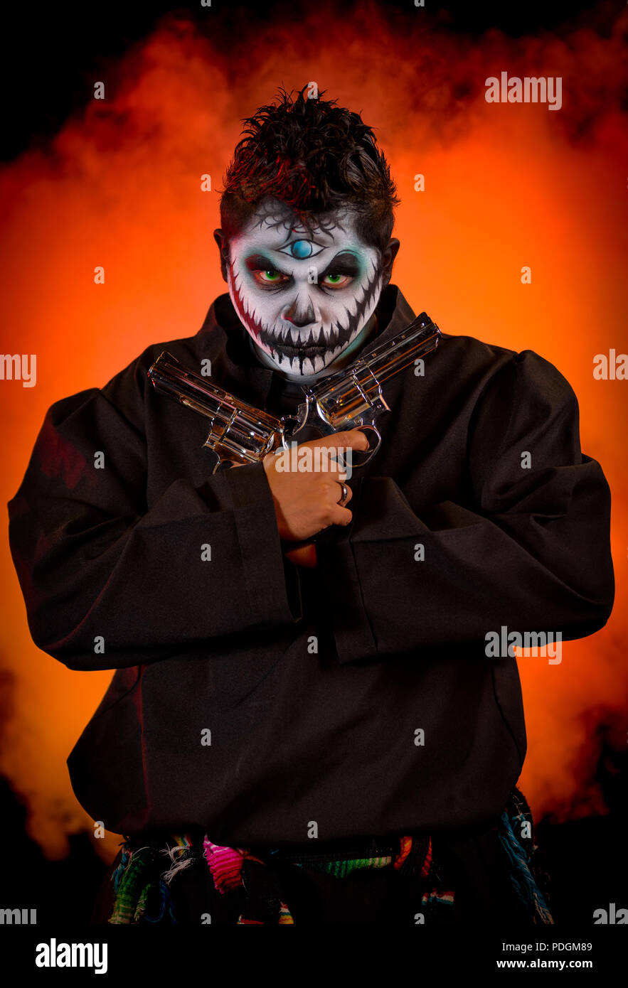 Un maschio latino modello con un moderno e in stile horror di approccio al dio Maya della malavita, Xibalba. Modello holding due pistole. Sparato contro un bl Foto Stock