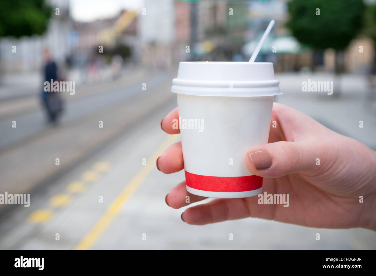 Mano femminile in possesso di una carta di tazza di caffè in una fermata del tram. Concetto di tenere lontano il caffè e il pendolarismo Foto Stock