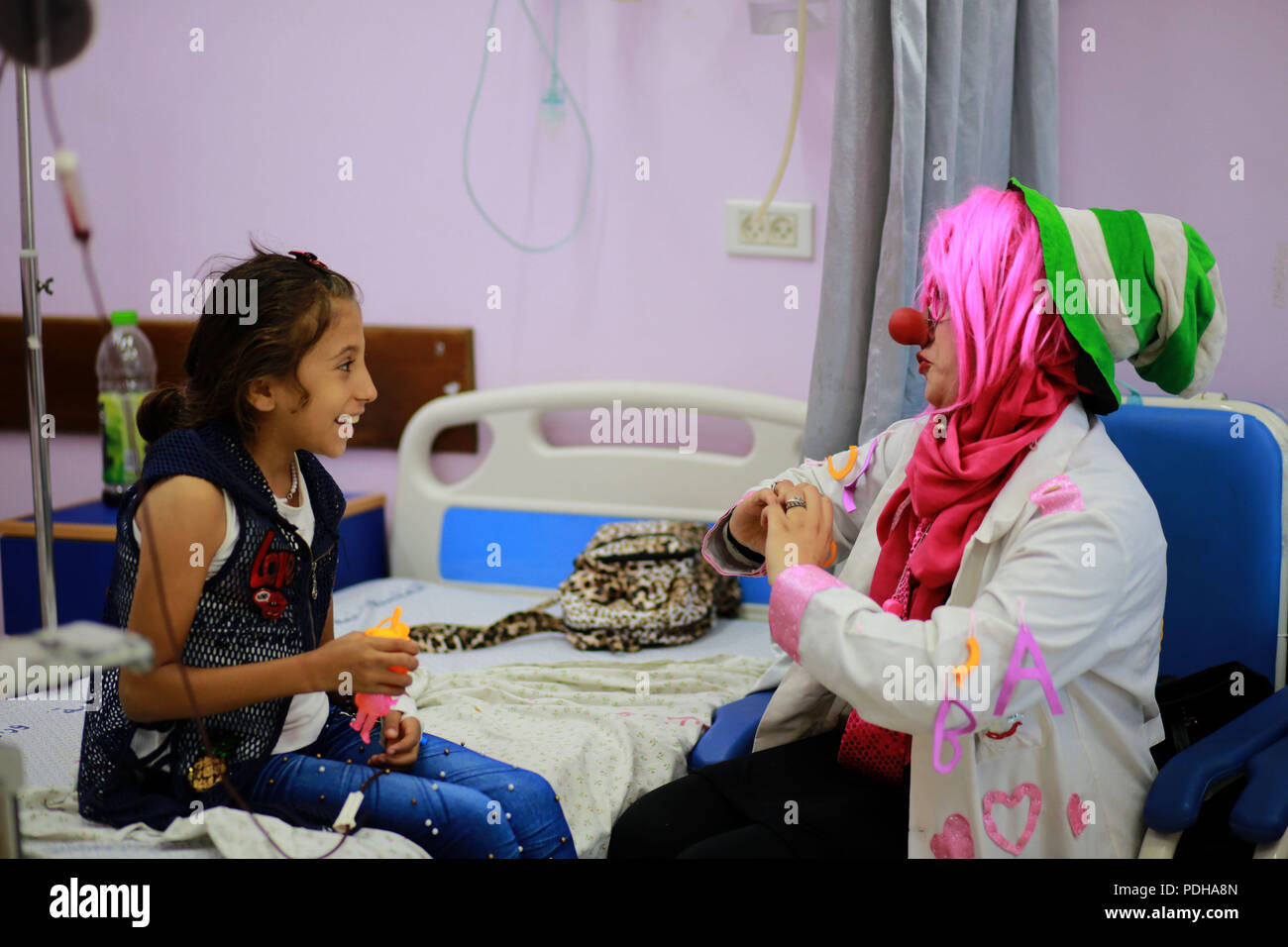 La striscia di Gaza. Il 9 agosto, 2018. Dina Nassar (R), intrattiene una ragazza che è un paziente affetto da cancro, nel suo costume da clown all'interno di un ospedale di Gaza City, e il Agosto 8, 2018. Cinque anni fa dopo il Dina's padre morì di cancro, ha iniziato a fare del volontariato in Basmit Amal associazione, una fondazione per la cura del cancro, servizio nella Striscia di Gaza. Ora Dina Nassar e un intero team di volontari svolgono i clown nel loro tempo libero per disegnare un sorriso ai bambini, labbra. Credito: Xinhua/Alamy Live News Foto Stock