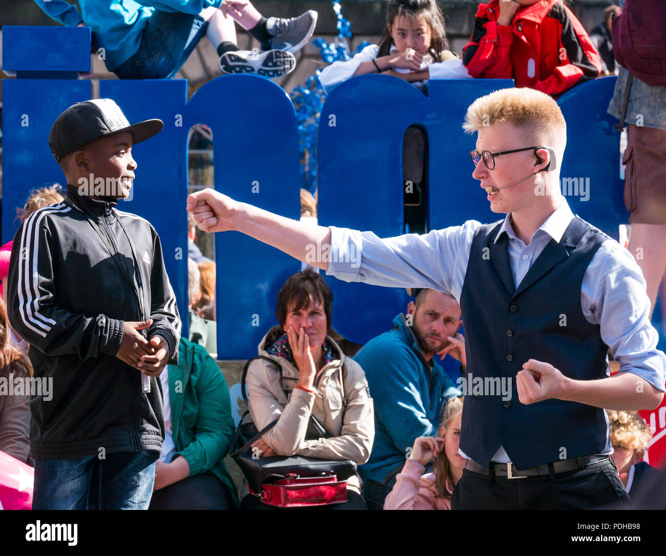 Edimburgo, Scozia, Regno Unito. Il 9 agosto 2018. Edinburgh Fringe Festival Royal Mile di Edimburgo, Scozia, Regno Unito. Su un soleggiato giorno del festival la Vergine denaro sponsorizzato street festival è gremita di gente ed esecutori della frangia. Una frangia street performer comporta un giovane ragazzo nero nel suo spettacolo di magia Foto Stock