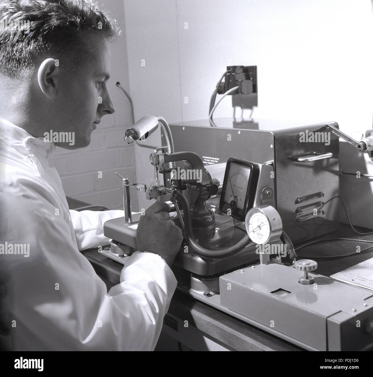 Degli anni Cinquanta, storico, scienziato maschio utilizzando attrezzature di collaudo ed il misuratore di tensione. Foto Stock