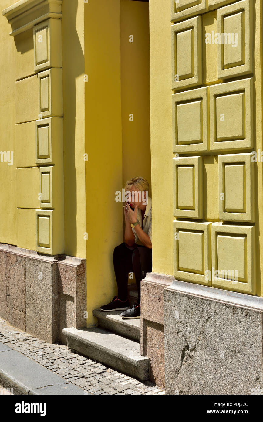 Donna Sigaretta fumare fuori seduta sul passo nella porta di colorato edificio giallo Foto Stock