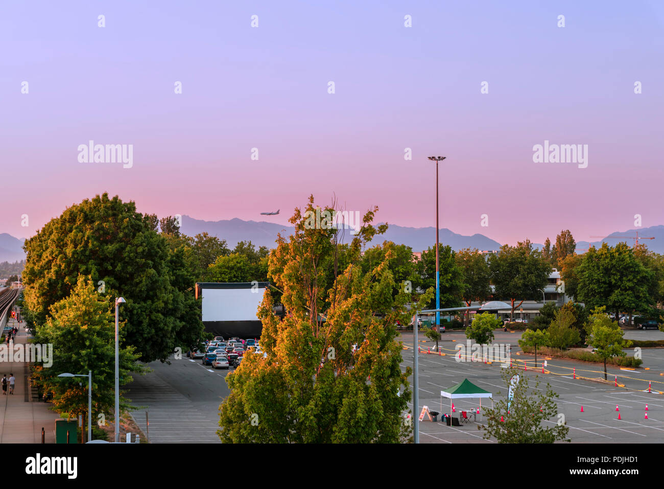 Parcheggio auto con cinema estate, verdi alberi, montagne, Battenti aereo, auto su una serata estiva in città moderna Foto Stock