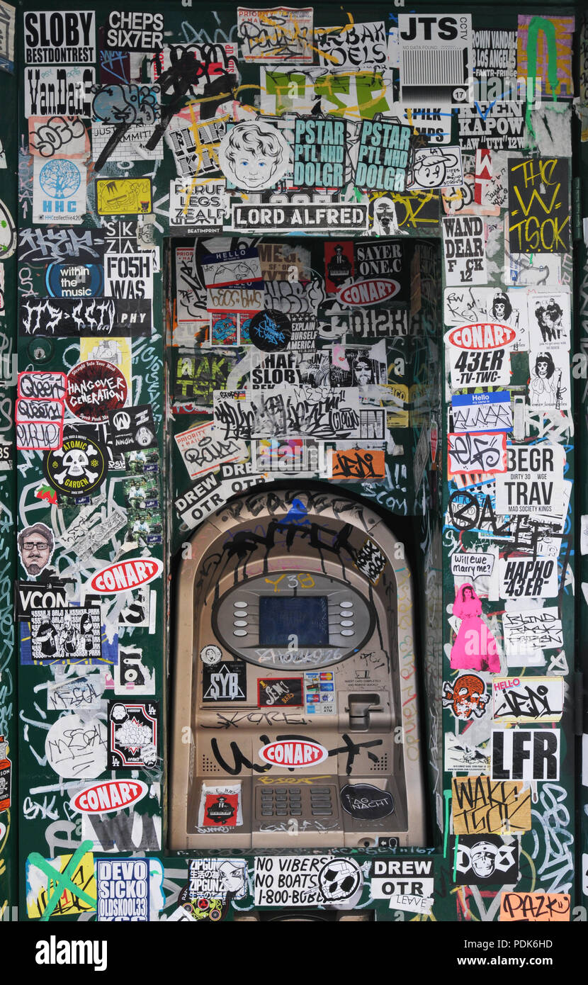 Adesivi e graffiti coprire un automatic teller machine nel quartiere delle Arti di Los Angeles, California. Foto Stock