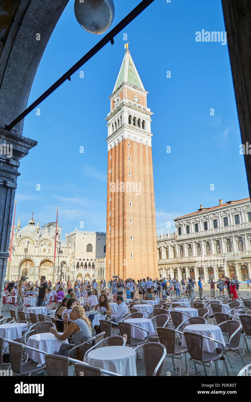 Piazza San Marco con il marciapiede tabella con le persone e i turisti si vede dal porticato, cielo blu in una soleggiata giornata estiva in Italia Foto Stock