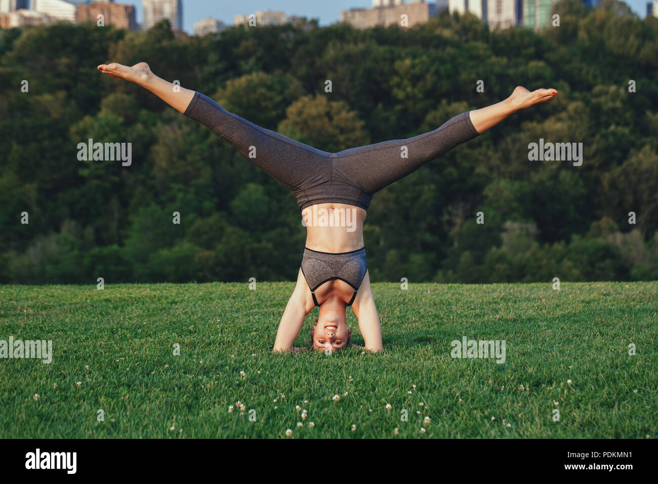 Giovane bella donna caucasica facendo yoga headstand pongono. Yogi donna facendo stretching allenamento nel parco all'aperto al tramonto. Un sano stile di vita moderno ac Foto Stock