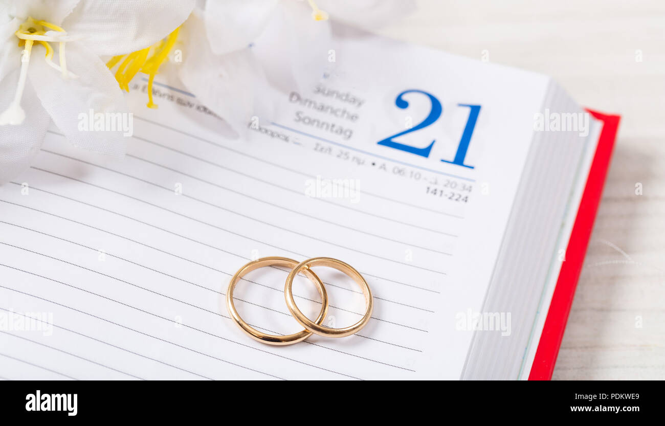 Pianificazione del concetto di matrimonio. Vista superiore del golden gli anelli di nozze e fiori su un calendario, su di un legno bianco tavolo. Foto Stock