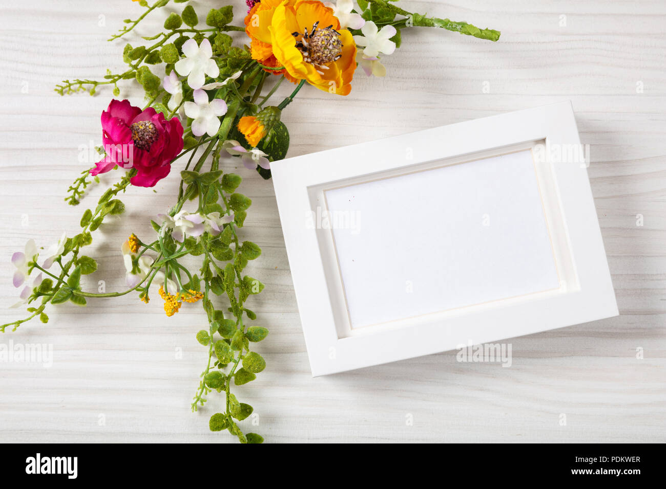 Mazzo di fiori e una casella vuota white photo frame, vista dall'alto, copia di spazio su un bianco sullo sfondo di legno. Foto Stock