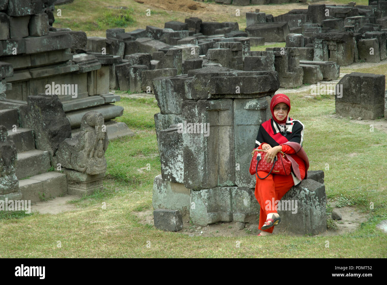 Signora in rosso sat su alcune pietre, Prambanan temple, Yogyakarta, Java, Indonesia. Foto Stock