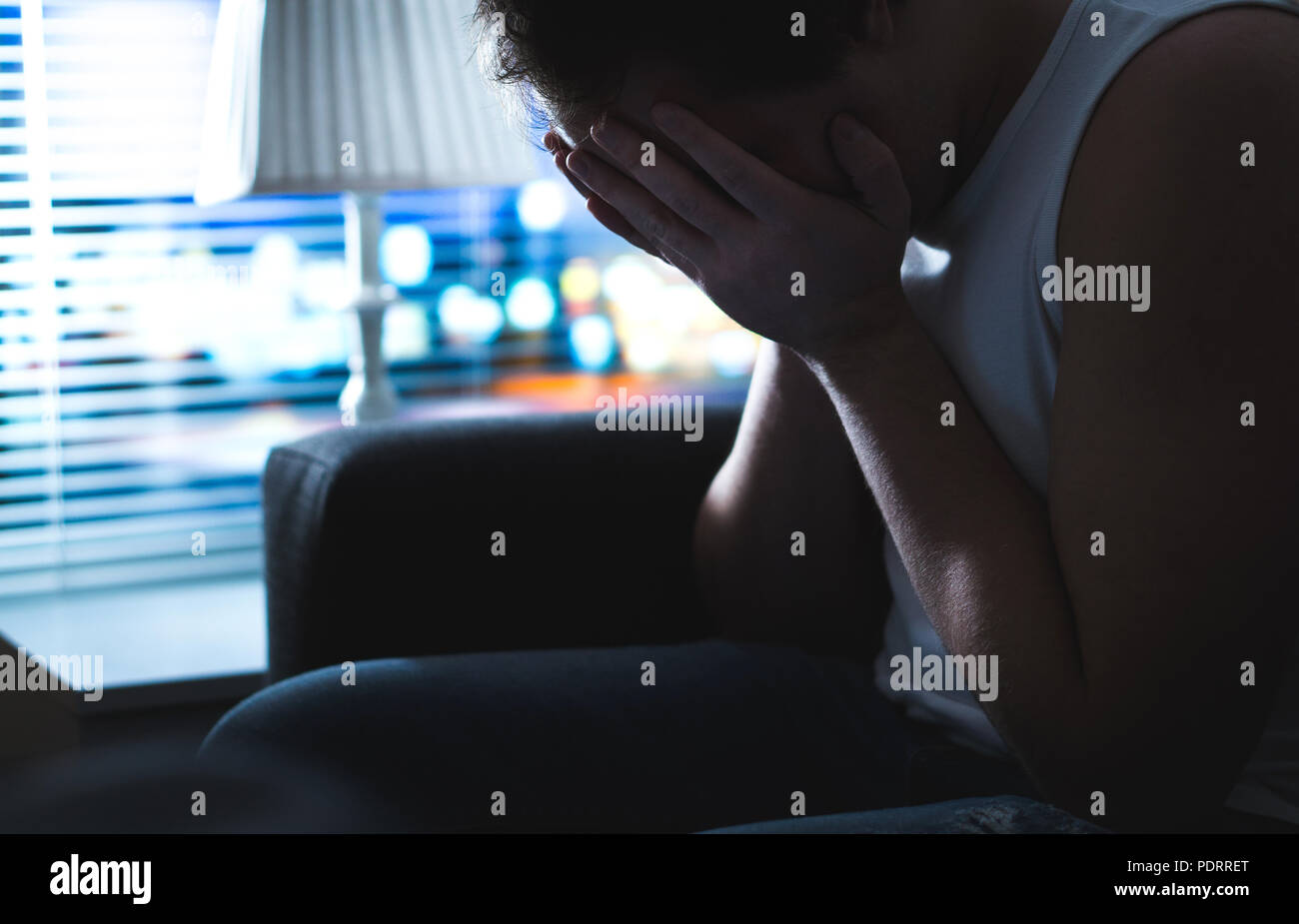 Triste e uomo infelice che ricopre la faccia con le mani nel buio dalla finestra. Burnout, sovraffaticamento o fallimento. Heartbroken persona mancante alla notte. Foto Stock