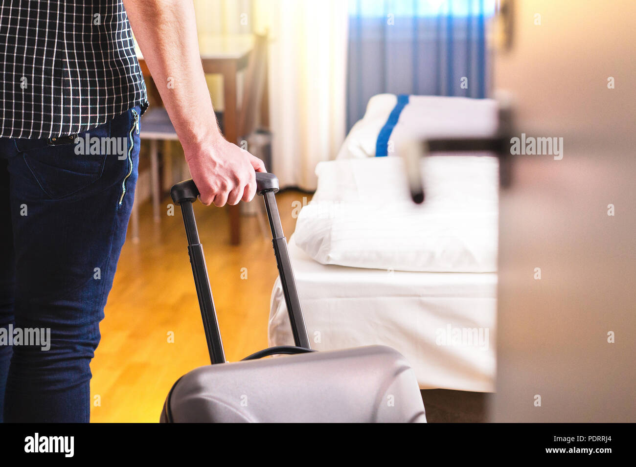 L'uomo tirando la valigia e entrando in camera d'albergo. Traveler che andando in camera o passeggiate all'interno di motel con bagagli. Viaggi e vacanze affitto appartamento. Foto Stock