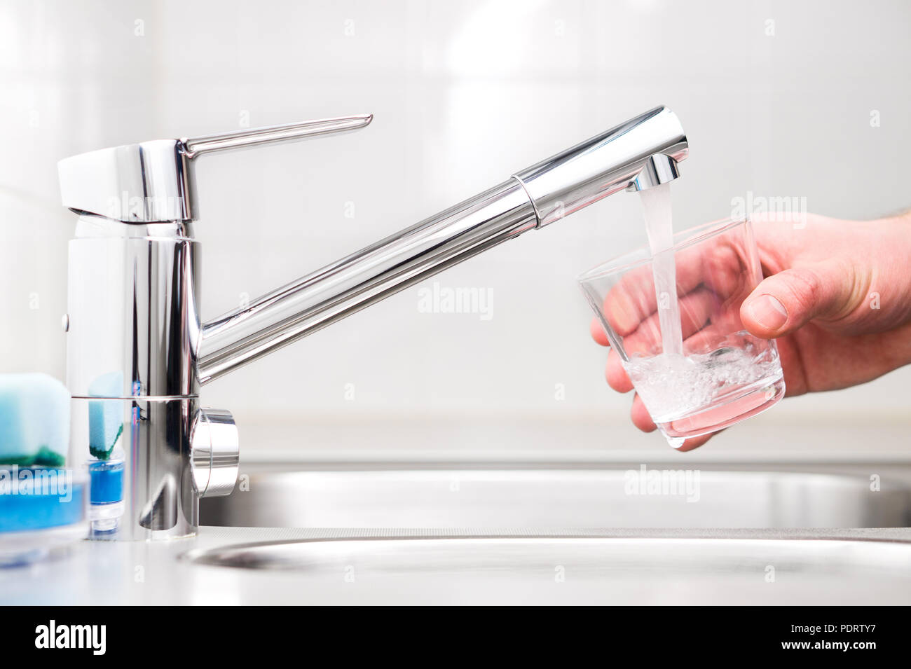 Il riempimento di vetro con acqua di rubinetto. Rubinetto moderno e lavello in cucina domestica. L'uomo versando bibite fresche alla tazza. Foto Stock