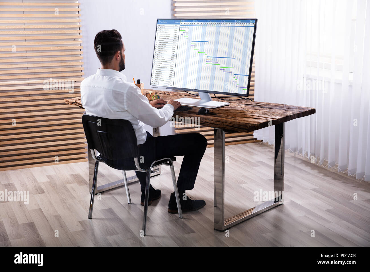 Giovane Imprenditore analizzando diagramma di Gantt sul computer sulla scrivania in legno Foto Stock