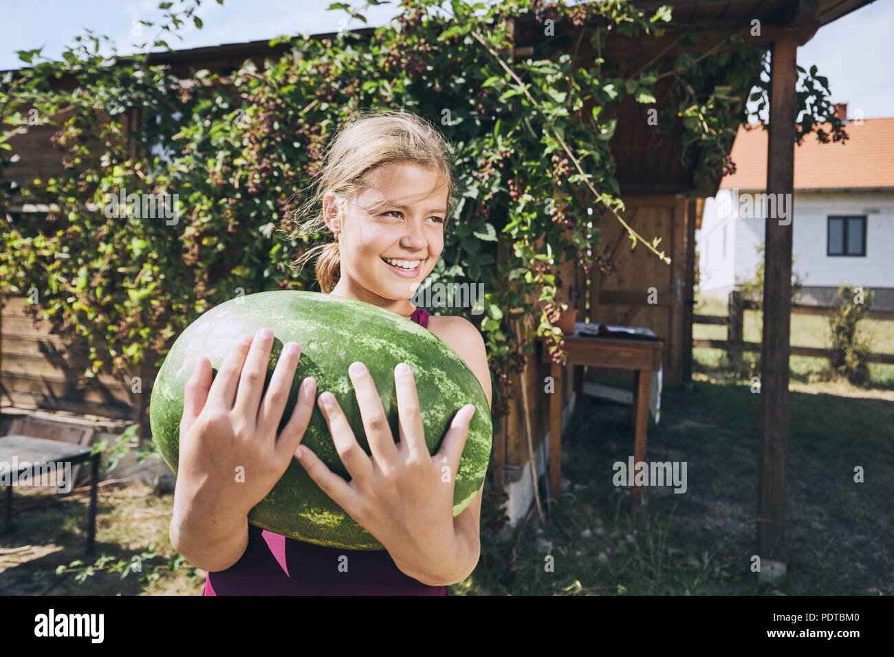 Ragazza ridere holding anguria pesante. Estate sul giardino sul retro della casa. Foto Stock