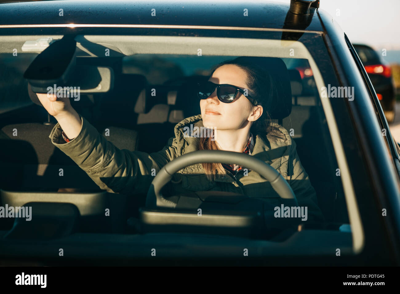 Ritratto di un giovane sorridente gioioso donna o ragazza conducente all'interno dell'auto. Lei sta per andare in retromarcia e regola il finestrino posteriore per vedere meglio. Foto Stock