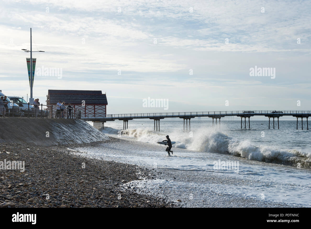 Surfer emergente dal mare a cambs, North Yorkshire, Inghilterra. La gente a guardare le onde del mare parete. Foto Stock