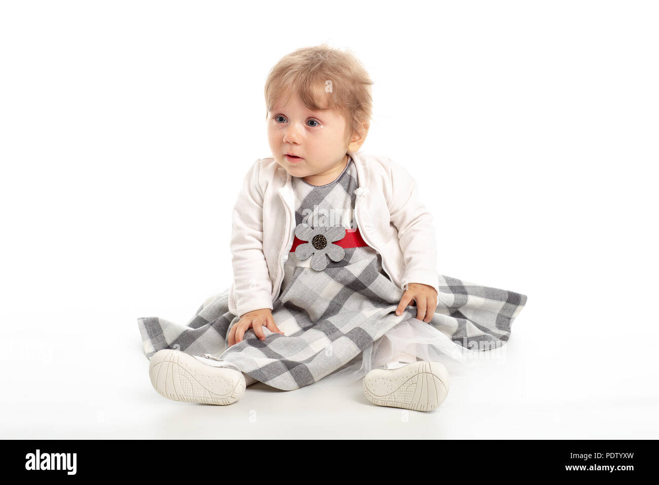 Eleganti bambina 1 anno vecchio seduto sul pavimento in studio. Sfondo bianco. Foto Stock