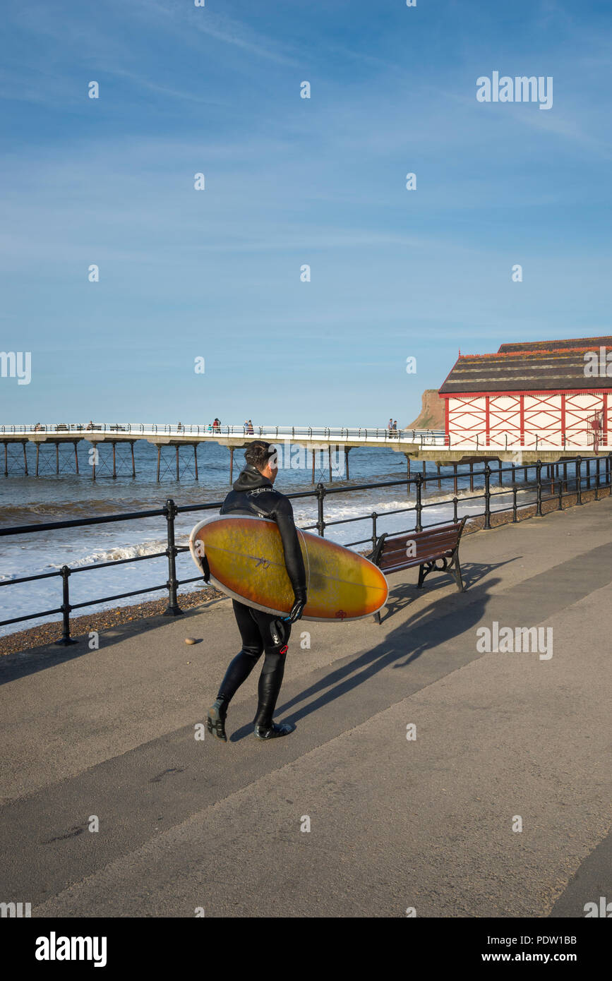 Giovane maschio surfer di ritorno dopo il tempo sulle onde a cambs sulla costa del North Yorkshire, Inghilterra. Foto Stock