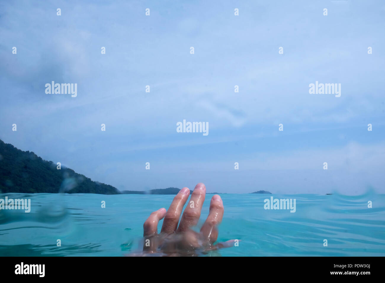 A cinquanta anni di donna metà mano sott'acqua in mare e le dita sopra l'acqua dietro è il blu del cielo e il verde degli alberi Foto Stock