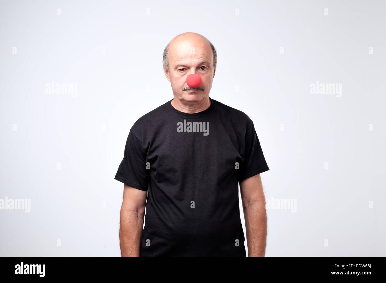Senior man in black tshirt in piedi con red clown naso in depressione. Egli soffre di essere soli. Foto Stock Senior man in black tshirt in piedi con red clown naso in depressione. Egli soffre di essere soli. Foto Stock