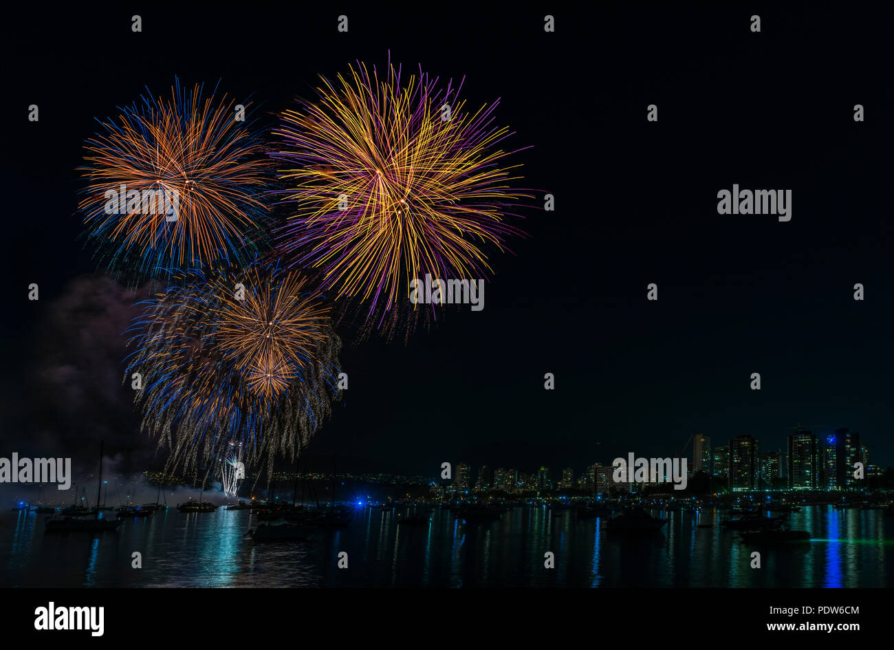 Lampeggia colorato di notte i fuochi d'artificio sull'oceano con galleggiante yacht e navi nei pressi di una grande città moderna con edifici alti Foto Stock