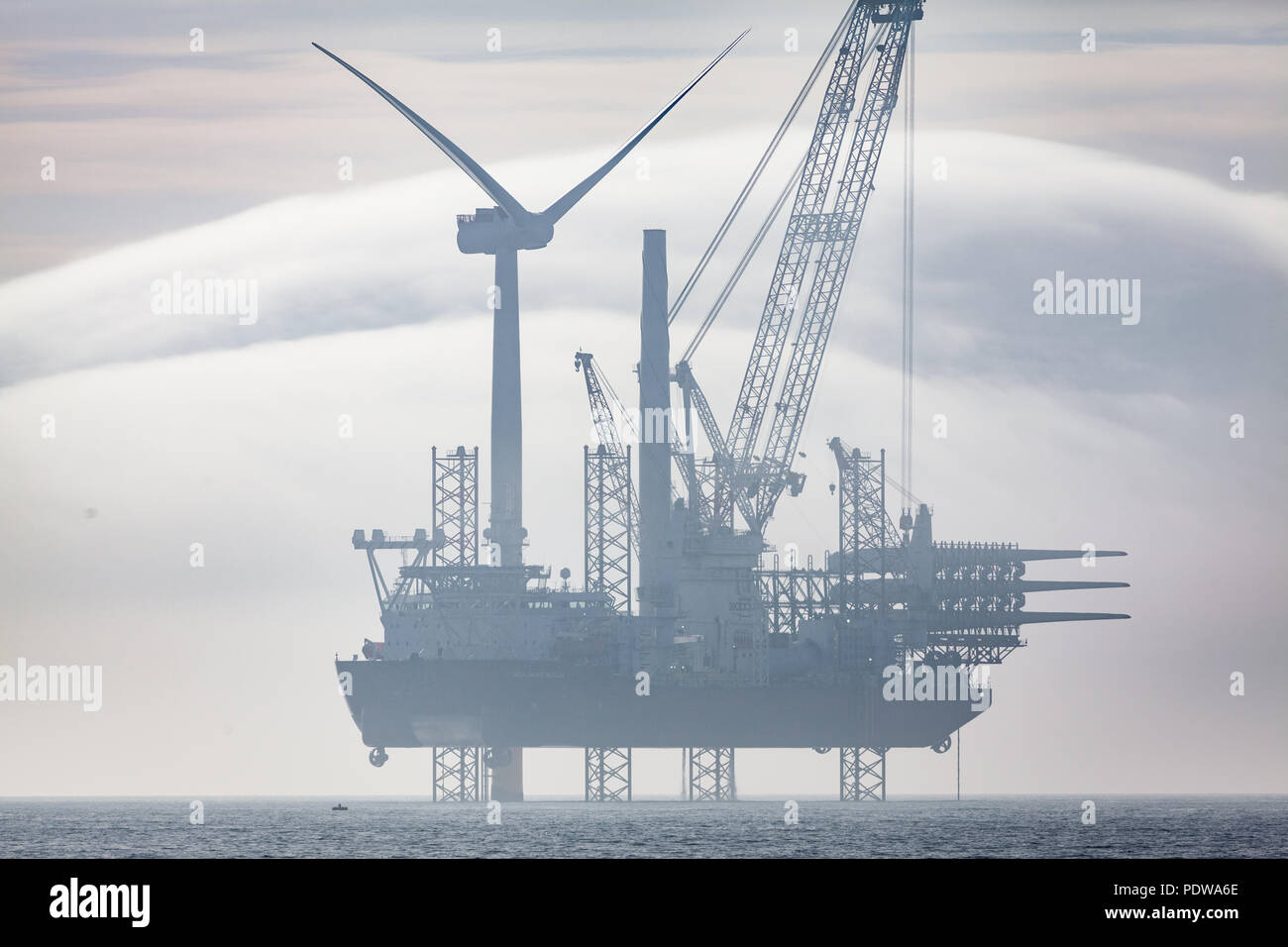 Seajacks Scilla lavorando sul Walney Estensione del parco eolico offshore in condizioni di nebbia. Coperta di insolito-come formazioni di nubi è possibile vedere in lontananza Foto Stock