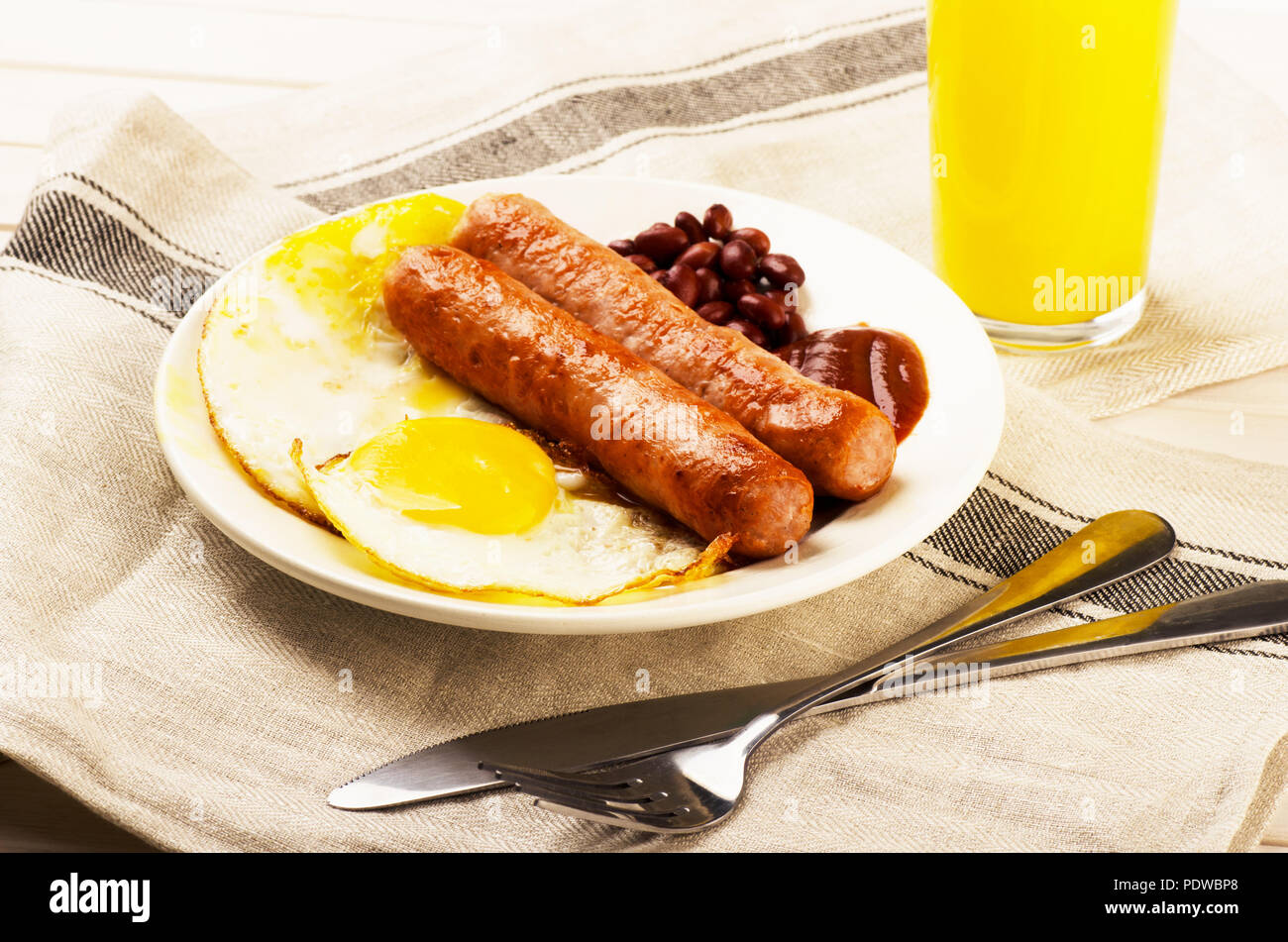 Una deliziosa prima colazione. Servita su un tavolo di legno con uova, salsicce, succo di arancia, coltello, forchetta. Foto Stock