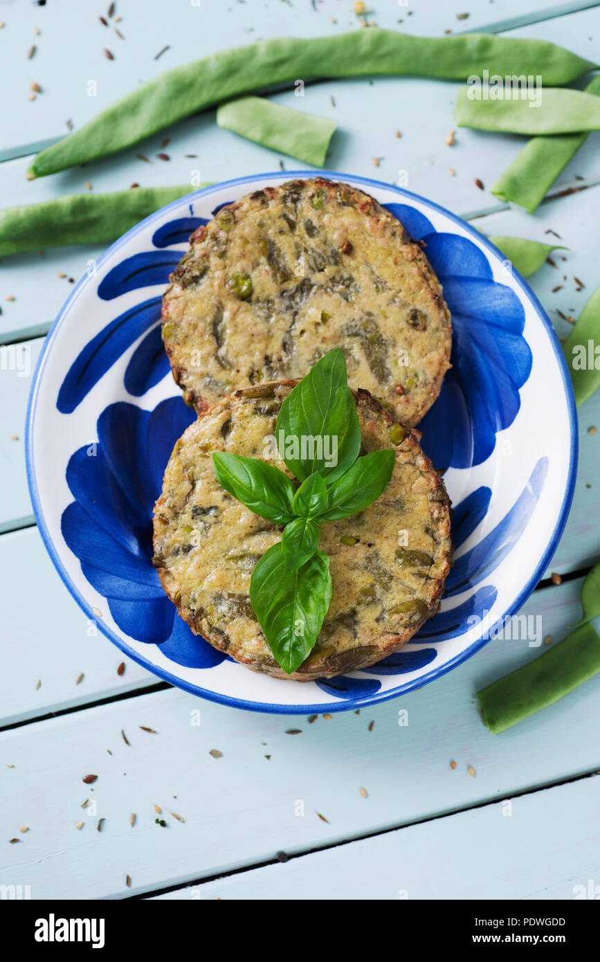 Angolo di alta vista di alcuni veggie hamburger con fagiolini e altre verdure in un bianco e blu della piastra ceramica, posto su una verde pallido woo rustico Foto Stock