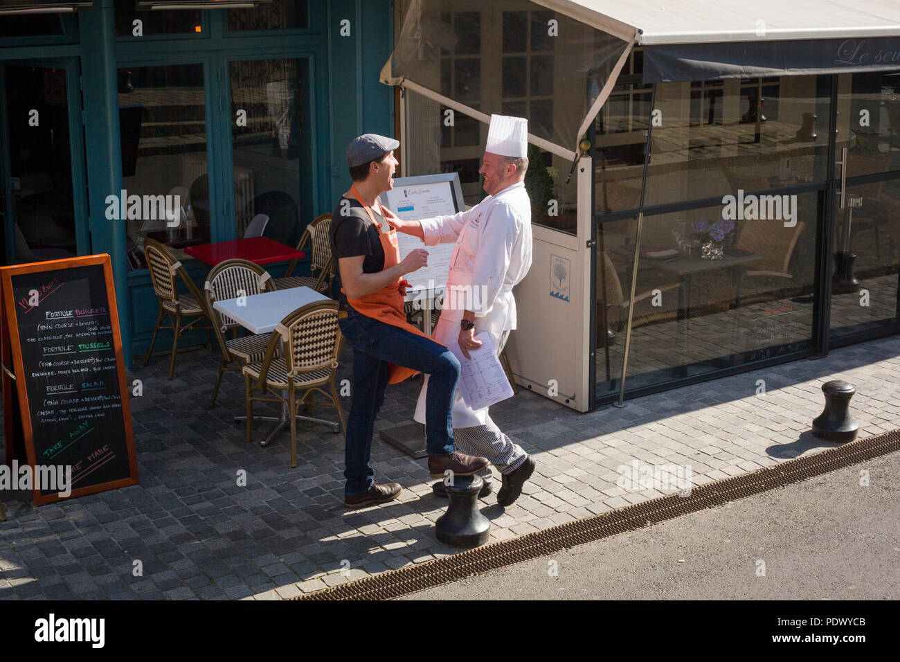 Uno chef gode di una barzelletta con un amico in una scena di strada in Honfleur, Normandia, Francia Foto Stock