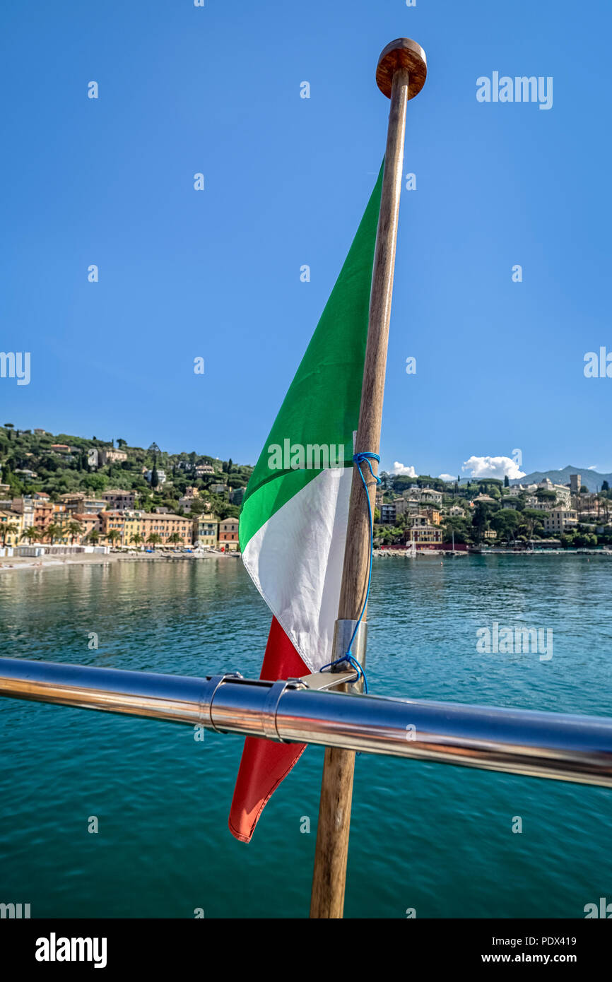 Bandiera italiana sul retro di una barca con la costa mediterranea sullo sfondo - da utilizzare come sfondo Foto Stock