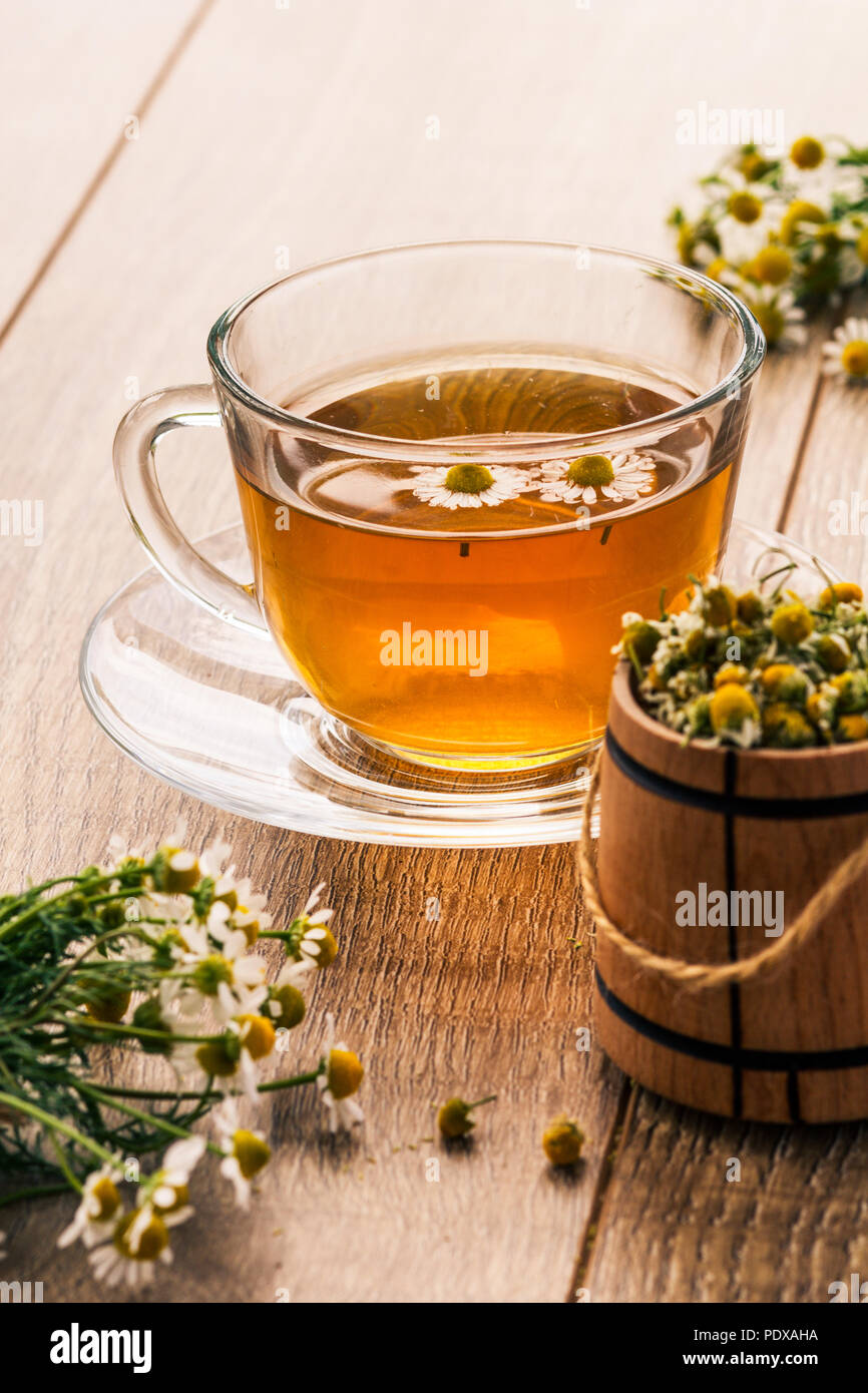 Bicchiere di vetro del tè verde con il bianco i fiori di camomilla e  piccolo barile di legno secco con fiori di camomilla in primo piano.  Profondità di campo Foto stock 