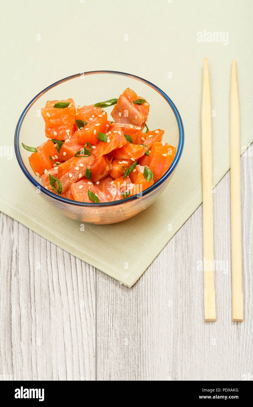 Salmone Hawaiian poke con cipolle verdi e i semi di sesamo in recipiente di vetro con bacchette sul tovagliolo. Vista da sopra con copia spazio. Organici di frutti di mare Foto Stock