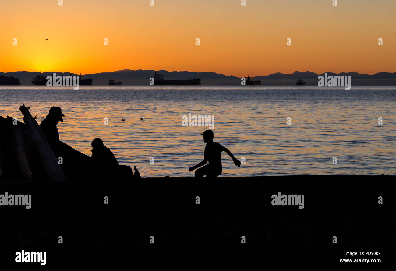 Tre bambini guardando fuori attraverso l'acqua verso il tramonto. Foto Stock