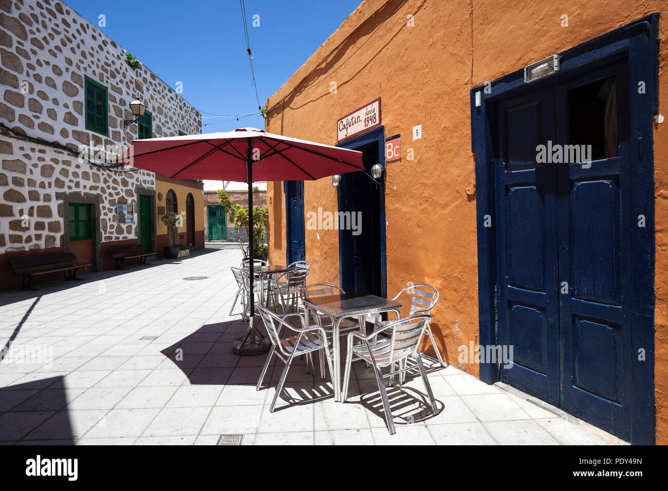 Tavolo e sedie a sdraio di fronte ad un cafe, case colorate, La Atalaya, Gran Canaria Isole Canarie Spagna Foto Stock