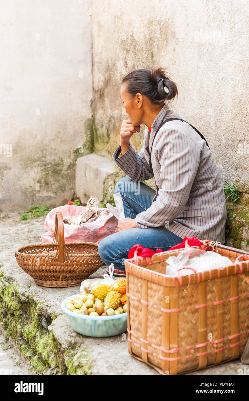 Donna vendita di verdure, carni e spezie, visualizzata al di fuori di un piccolo negozio. Sapori locali e cibi esotici in un affollato mercato di villaggio in Asia. Foto Stock