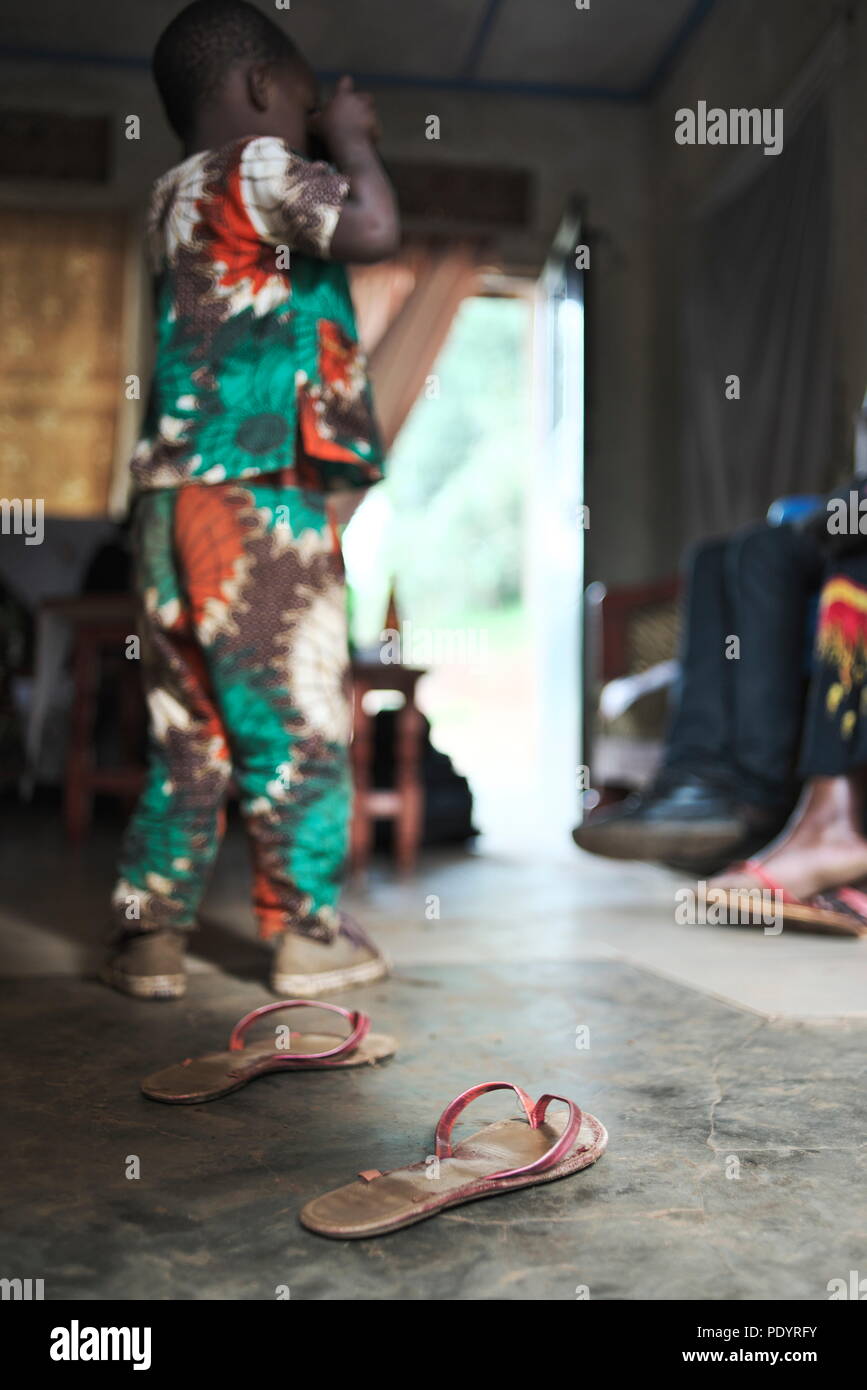 Giovani Africian bambino sta in casa rurale in Uganda e scatta una fotografia utilizzando una fotocamera con le scarpe sul pavimento Foto Stock