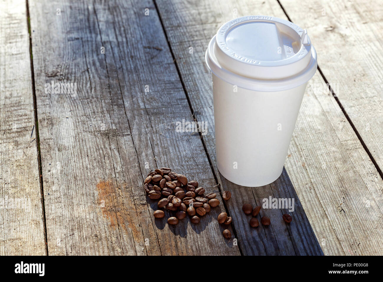 Bicchiere di carta e i chicchi di caffè su sfondo di legno Foto Stock