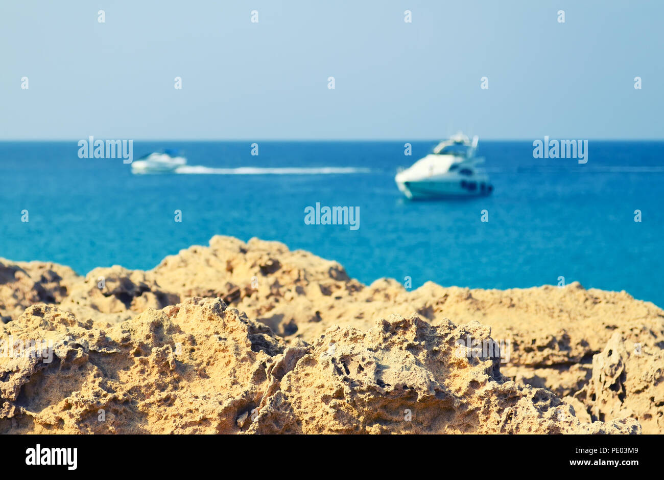 La roccia vulcanica su uno sfondo sfocato del blu del mare e le barche Foto Stock