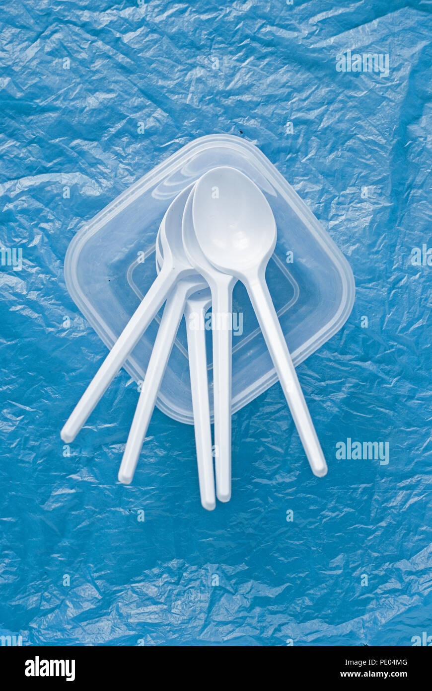 Set di bianco cucchiai di plastica in un contenitore di plastica su un blu sacchetto di plastica Foto Stock