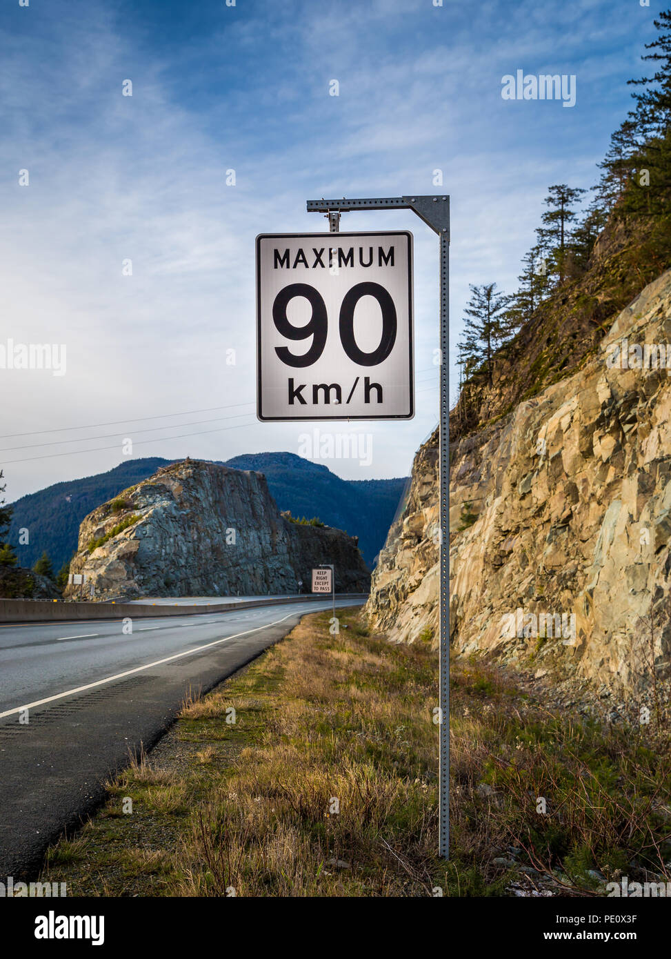 Segnale di limite di velocità con un tenere la destra sign in background accanto ad una strada di montagna. Foto Stock