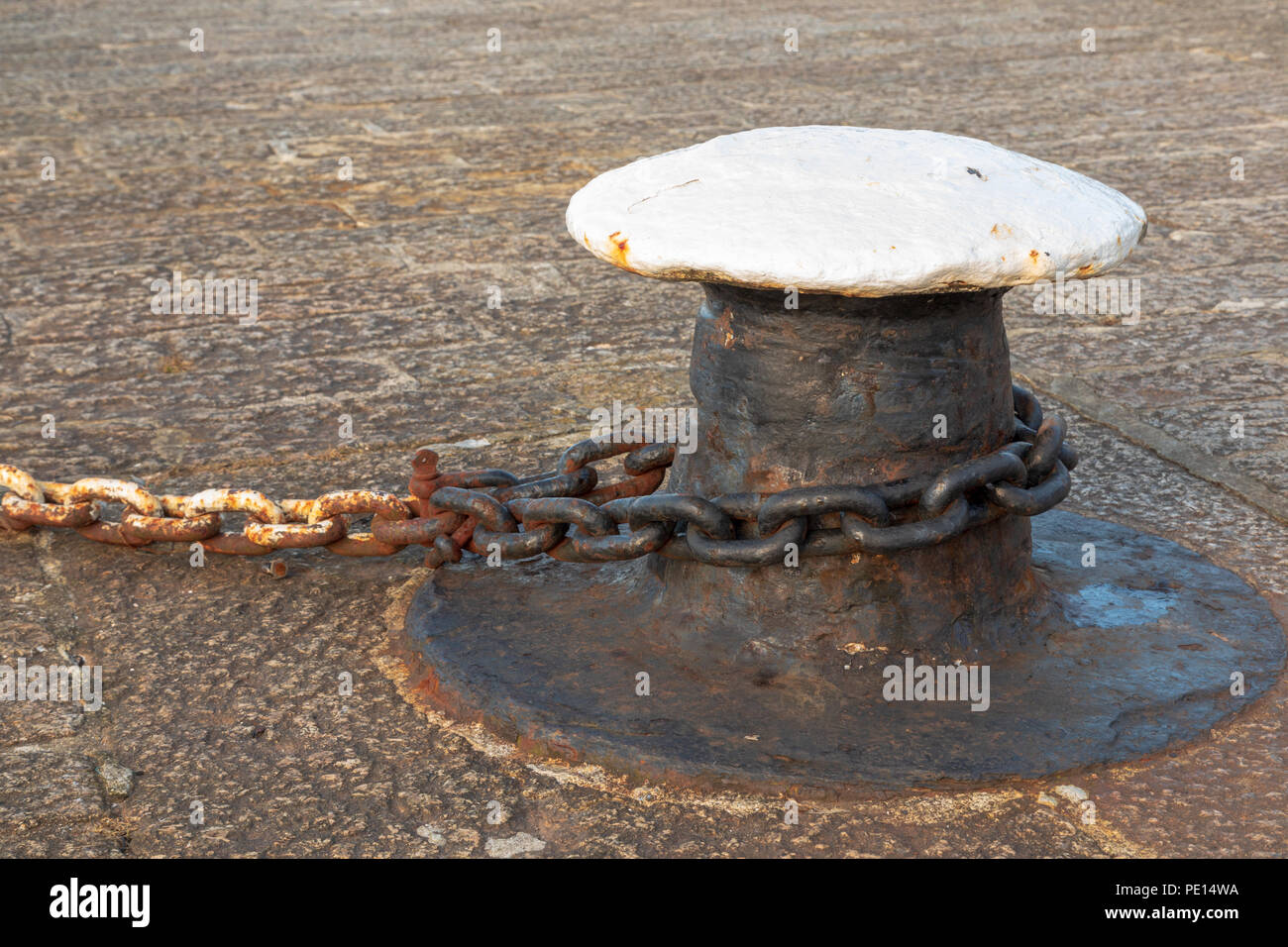 Mooring bollard con rusty catena fissata attorno ad esso su una banchina di un porto Foto Stock