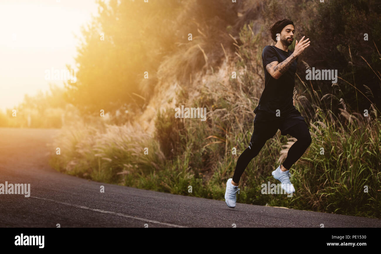 Montare il giovane uomo che corre veloce su strada di montagna. Atleta in volata su strada all'esterno. Foto Stock