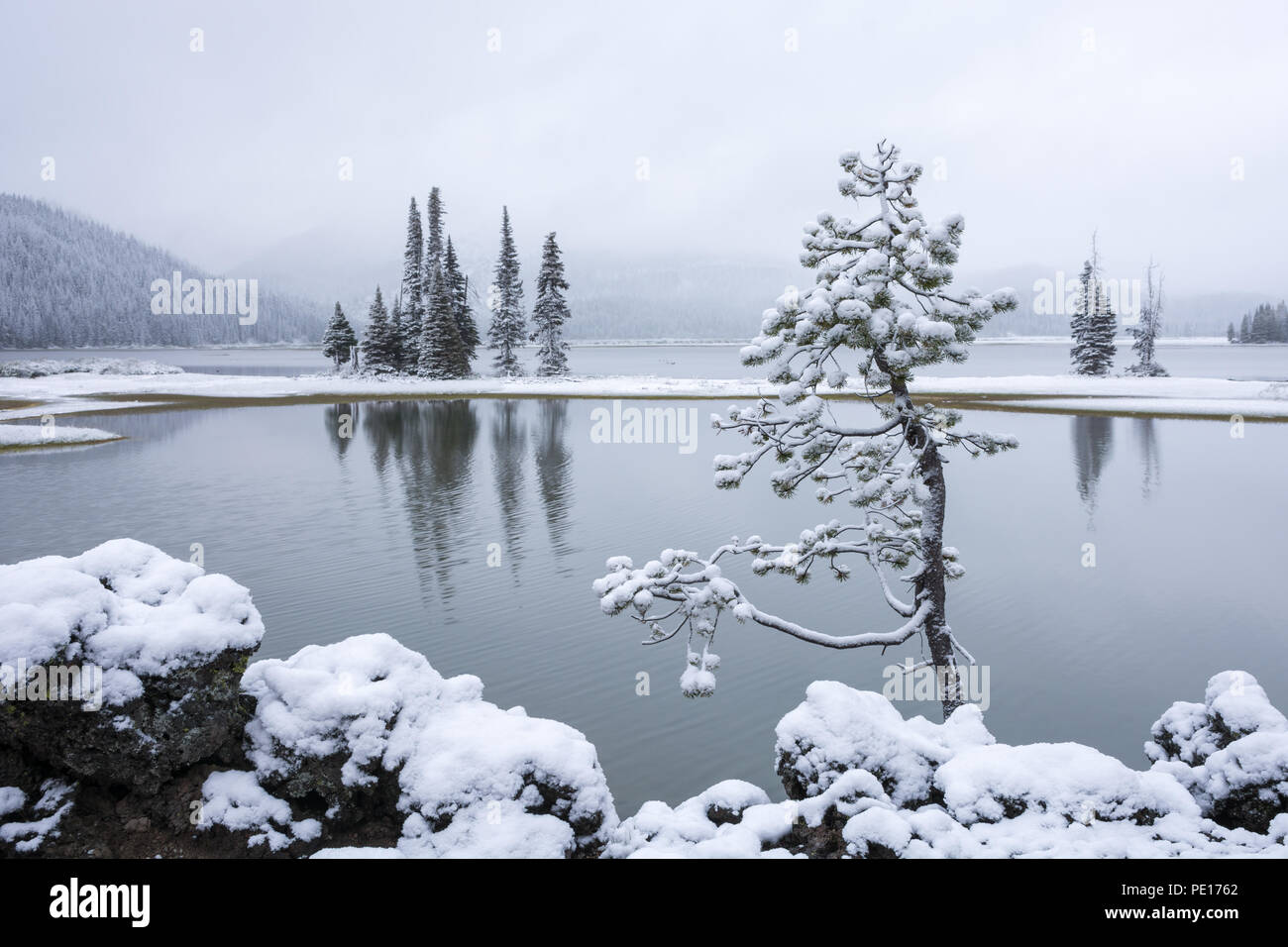 Una leggera nevicata che copre gli alberi, rocce e montagne che circondano il lago di scintille in Oregon centrale su un inizio di mattina di giugno. Foto Stock